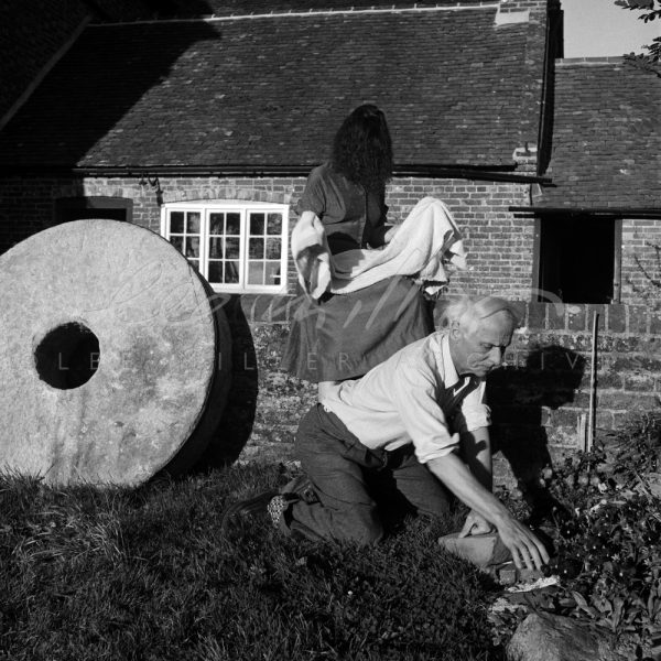 Dorothea Tanning drying her hair and Max Ernst gardening, next to a large Mill grindstone.