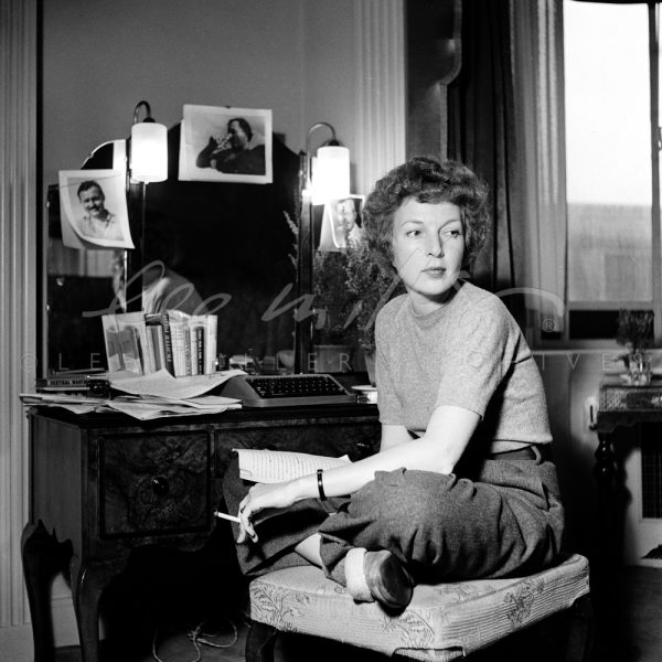 Black and white. Martha Gellhorn sits cross-legged by her dressing table.
